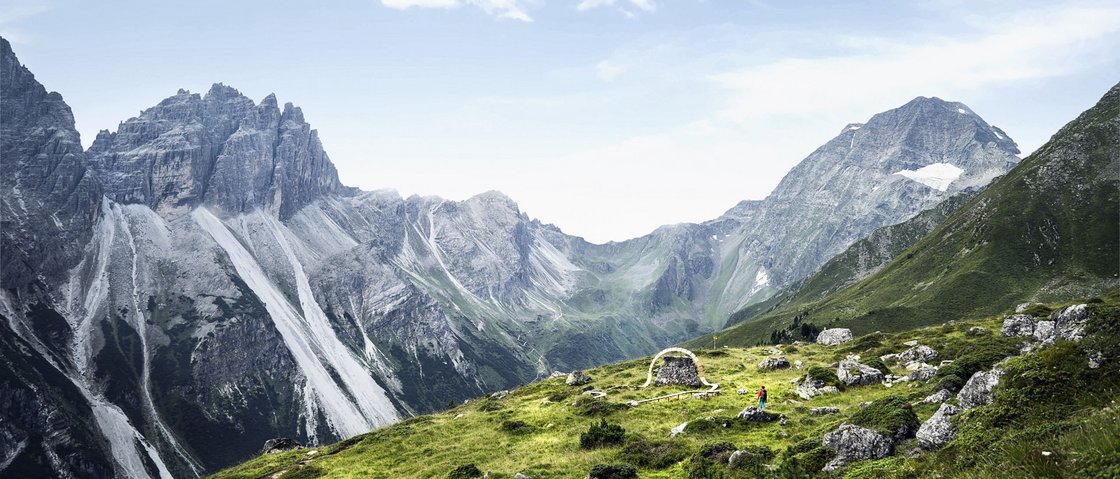 Love for nature at our hiking hotel in Stubaital Mountain landscape with green hill, rocks, and steep cliffs under blue sky