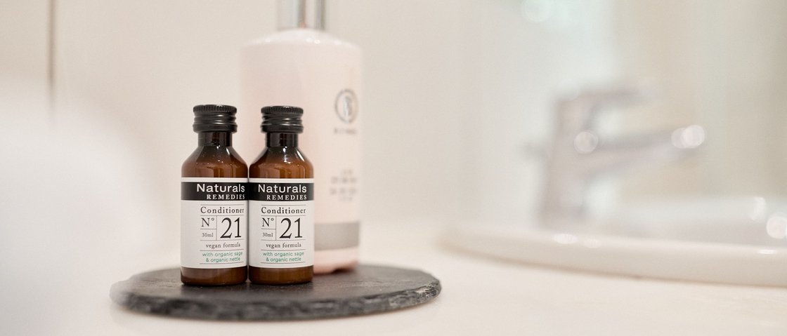 Unwind at our spa hotel in Stubaital Two small natural remedy conditioner bottles on a black coaster in the bathroom