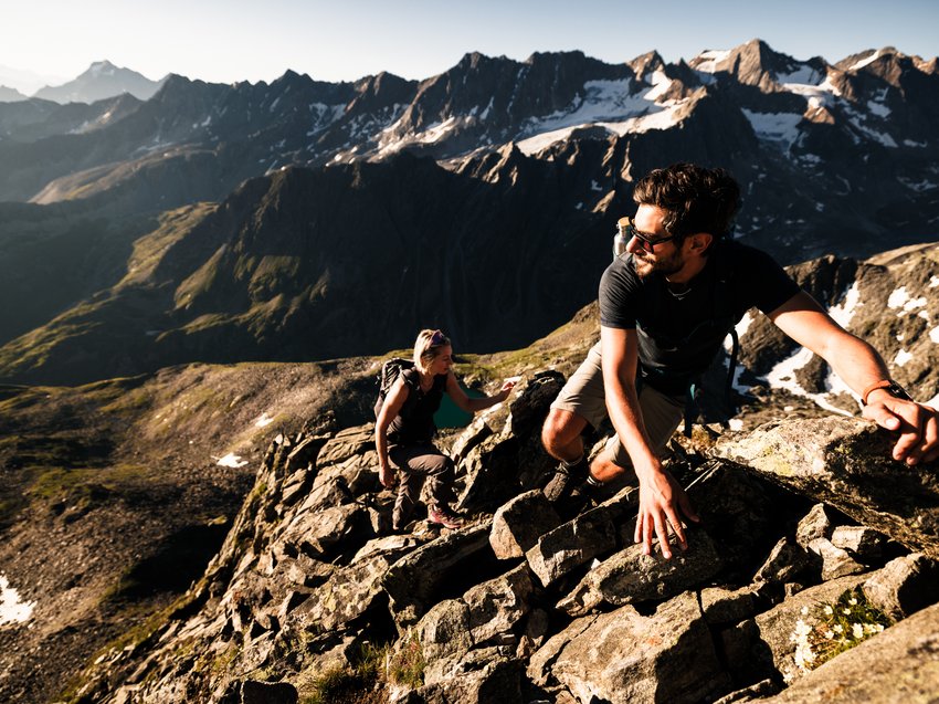 Naturliebe im Wanderhotel im Stubaital Zwei Wanderer klettern auf felsigem Bergpfad mit Alpen im Hintergrund bei Sonnenlicht