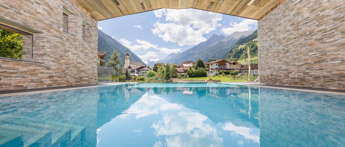 Rejuvenation at our 4-star wellness hotel in Tyrol Covered pool overlooking Alps, houses, and blue sky with clouds