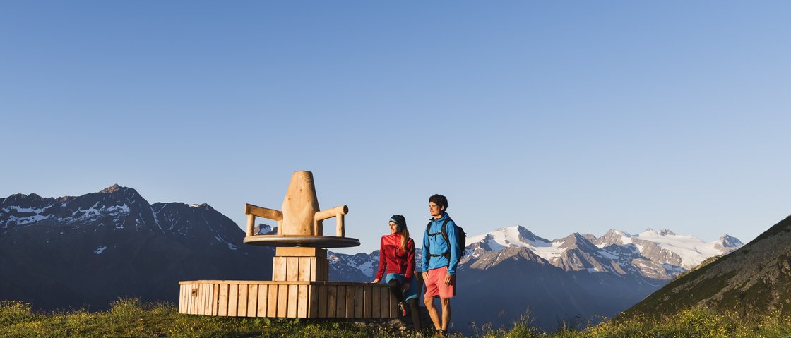 Naturliebe im Wanderhotel im Stubaital Zwei Wanderer neben einer großen Holzskulptur mit Alpen im Hintergrund