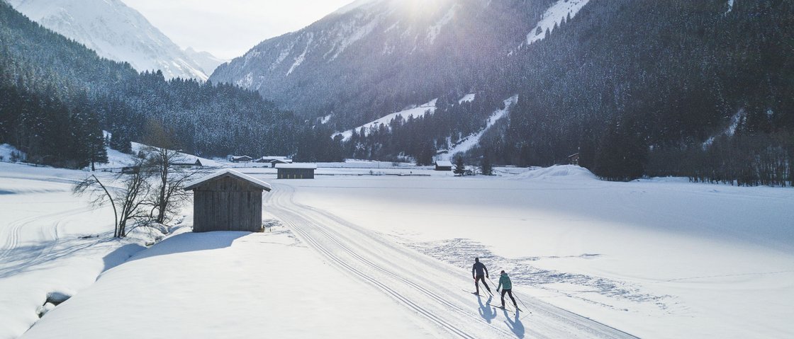 Dreaming of skiing? Head to our ski hotel in Stubaital! Two cross-country skiers in snowy valley with mountains and sun in background