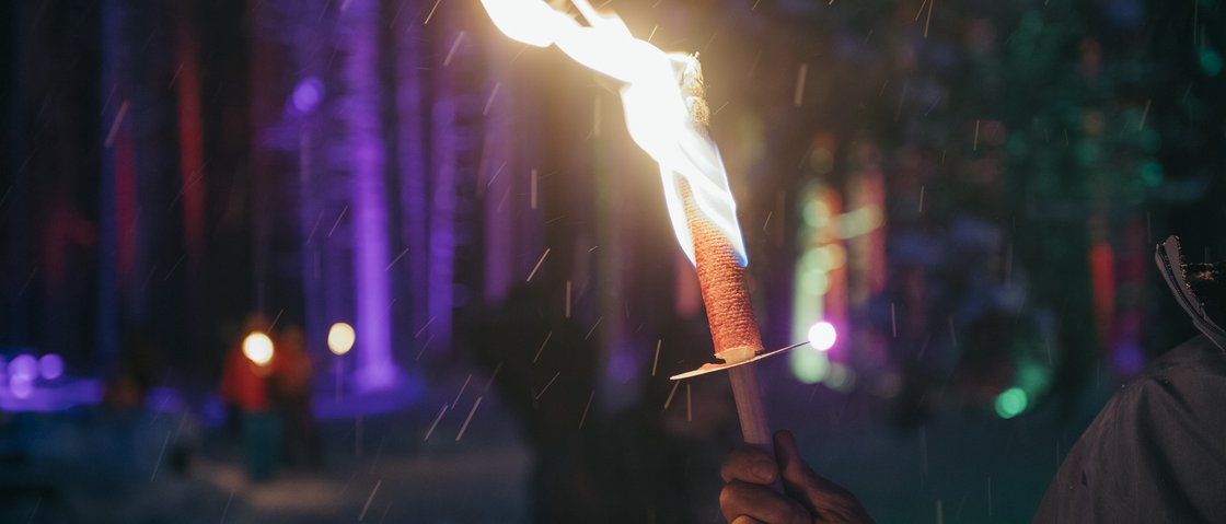 Das Plus im Skiurlaub im Stubaital Hand hält brennende Fackel bei Nacht mit buntem Hintergrund