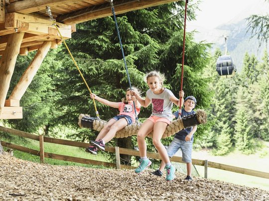 Qualitätszeit im Familienhotel im Stubaital Drei Kinder spielen auf einer großen Hängeschaukel im Wald