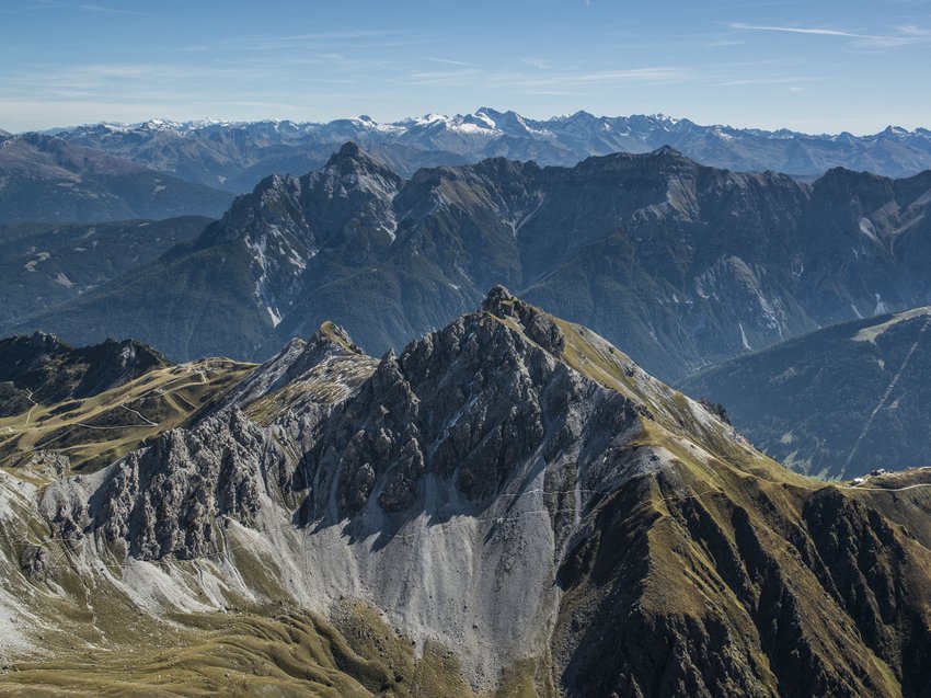 Bereit für Ihren Urlaub im Stubaital im Sommer? Bergkette mit schroffen Felsen und grün-braunen Wiesen unter blauem Himmel