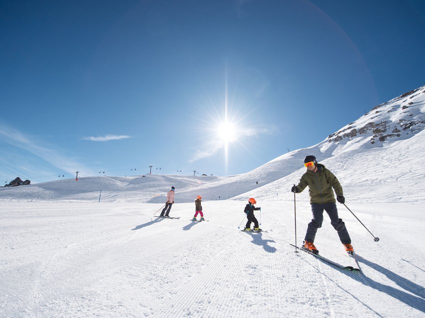 Qualitätszeit im Familienhotel im Stubaital Familie beim Skifahren an sonnigem Tag auf verschneitem Berg