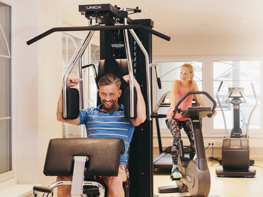 Fit bleiben im Sporthotel im Stubaital Mann trainiert an Fitnessmaschine, Frau fährt Fahrrad im Fitnessraum