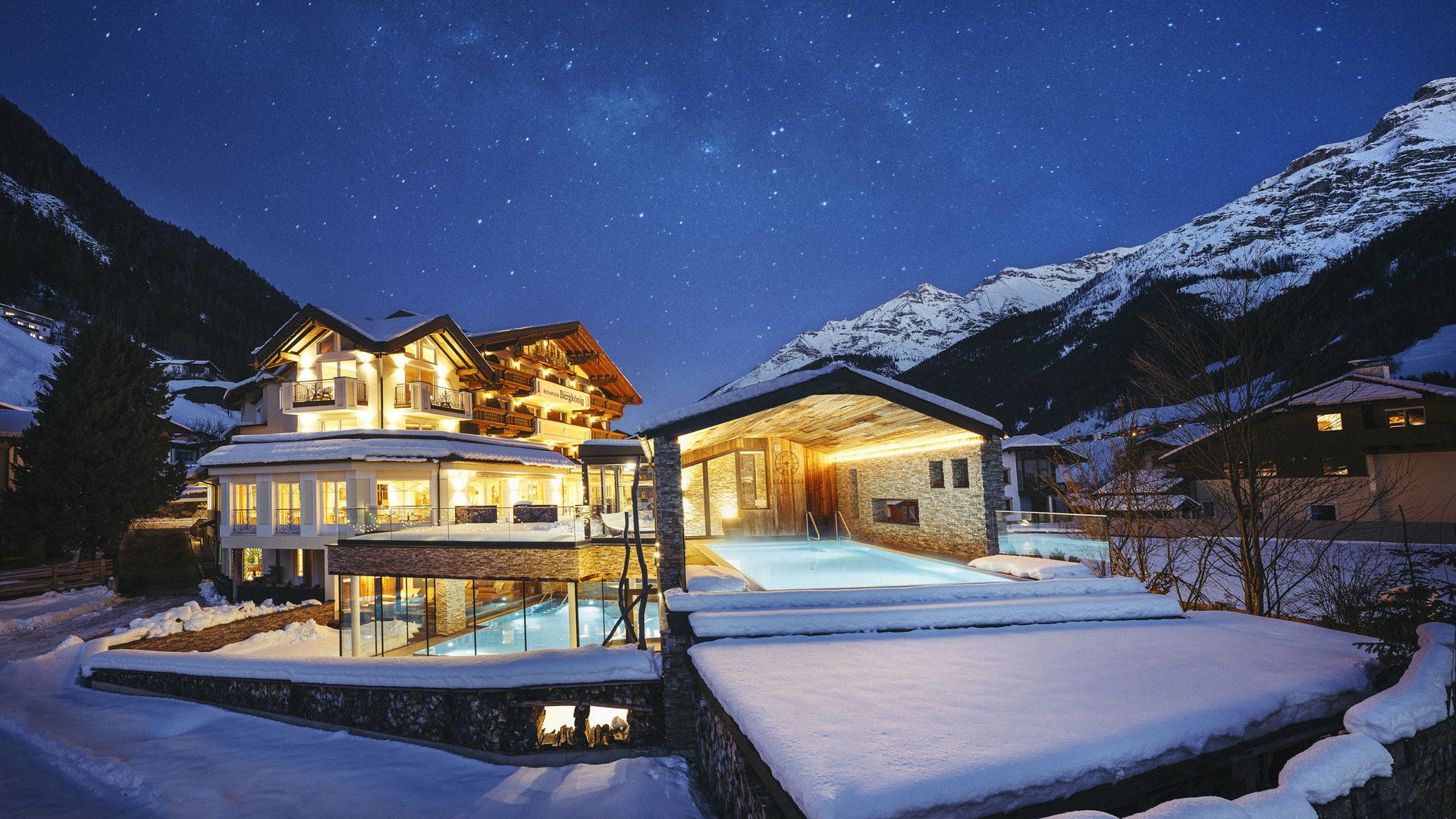 Hier finden Sie unser Hotel. Beleuchtetes Hotel mit Außenpool in verschneiter Berglandschaft bei Nacht