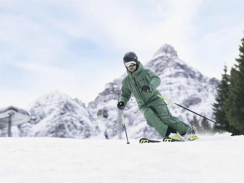 Dreaming of skiing? Head to our ski hotel in Stubaital! Skier in green gear skiing on snow with snowy mountains in the background