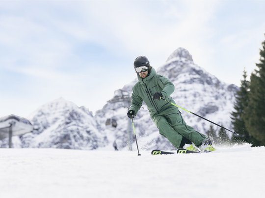 Dreaming of skiing? Head to our ski hotel in Stubaital! Skier in green gear skiing on snow with snowy mountains in the background