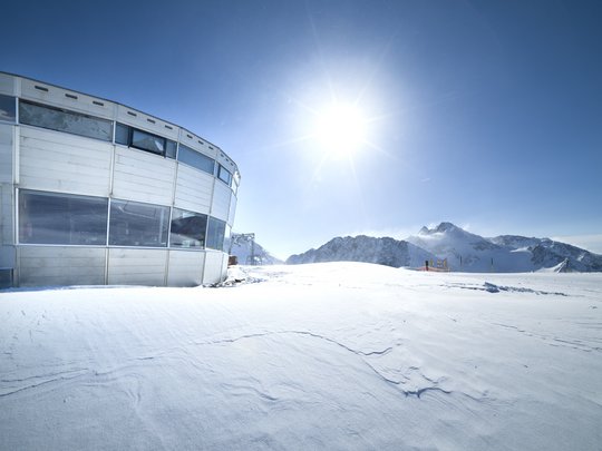 Dreaming of skiing? Head to our ski hotel in Stubaital! Snowy landscape with building and mountains under bright sunshine