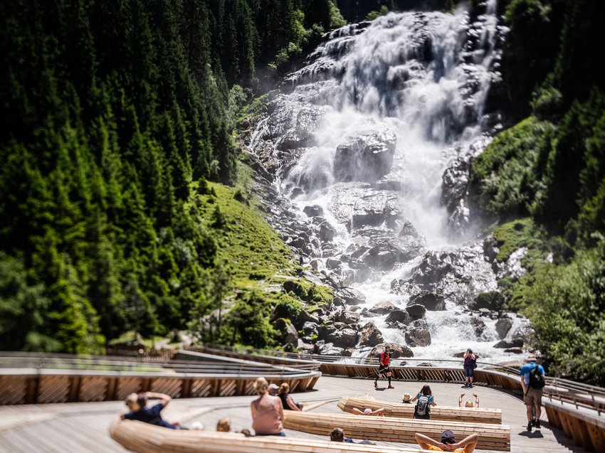 Recharge at our hotel in Neustift im Stubaital, Austria Visitors sitting and walking near a large waterfall in a forested valley
