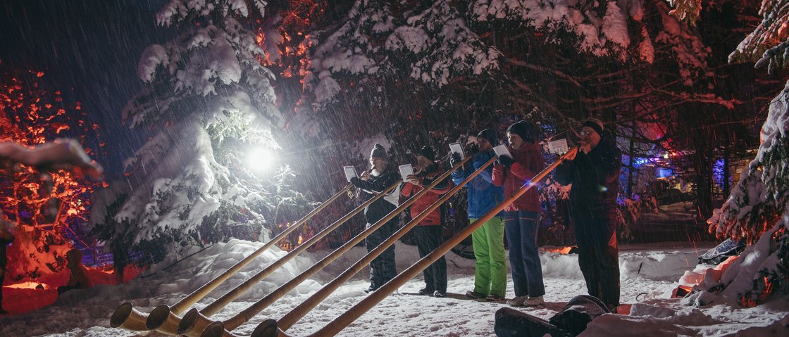Das Plus im Skiurlaub im Stubaital Menschen spielen Alphörner im Schnee in einem mit Lichtern beleuchteten Winterwald