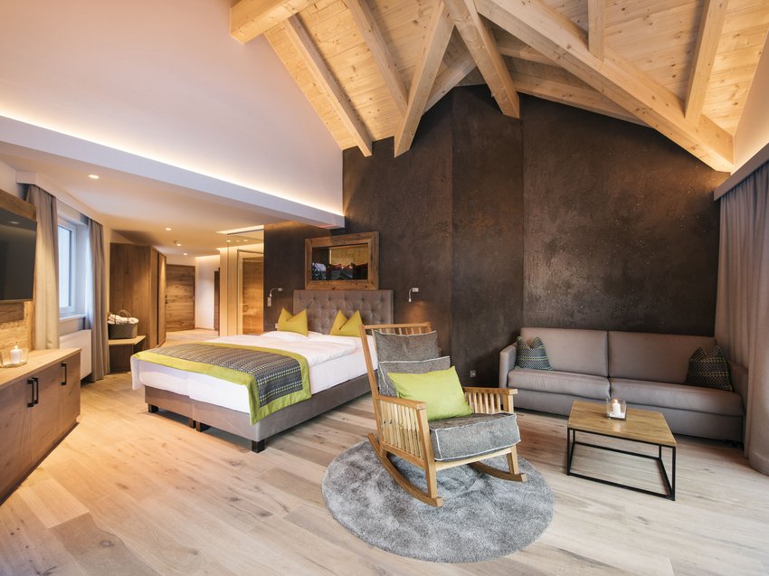 Recharge at our hotel in Neustift im Stubaital, Austria Modern hotel room with wooden furniture, bed, rocking chair, and sofa