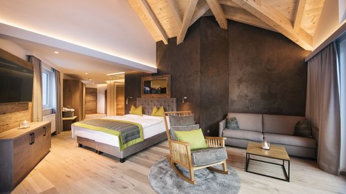 Massagen, Packungen und mehr im Bergkönig Modernes Hotelzimmer mit Holzmöbeln, einem Bett, Schaukelstuhl und Sofa