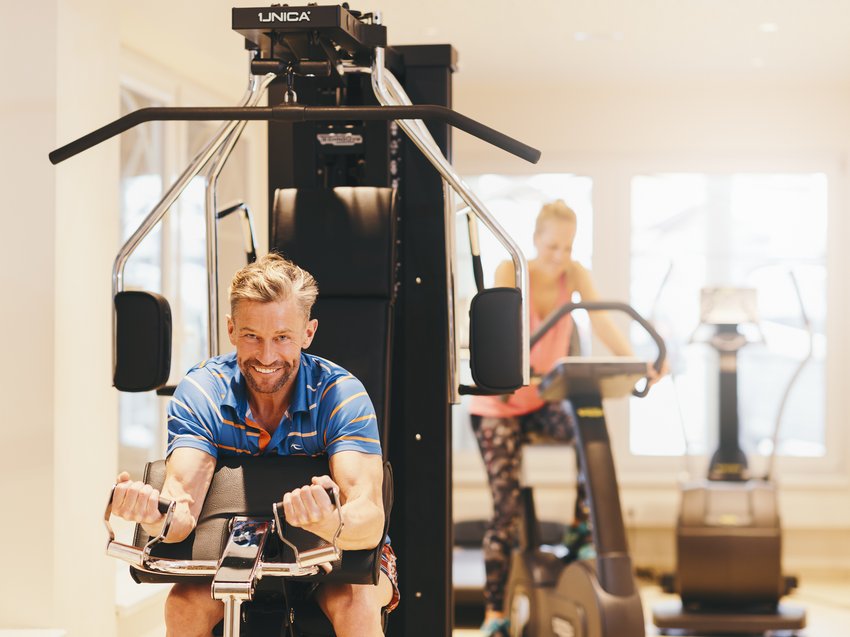 Unwind at our spa hotel in Stubaital Man using strength training machine, woman cycling on exercise bike in background