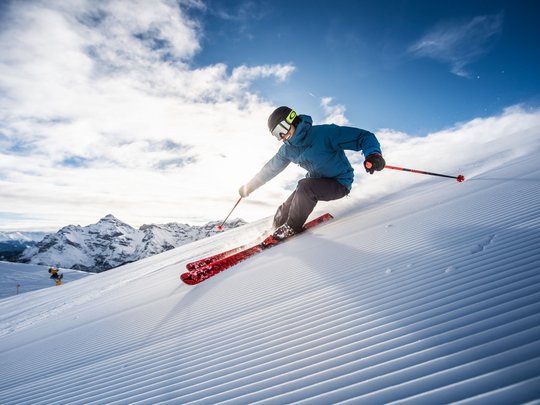 Dreaming of skiing? Head to our ski hotel in Stubaital! Skier carving on a groomed slope with mountains and blue sky in the background