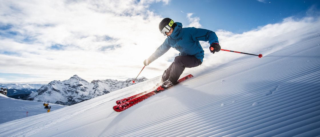 Dreaming of skiing? Head to our ski hotel in Stubaital! Skier carving on a groomed slope with mountains and blue sky in the background