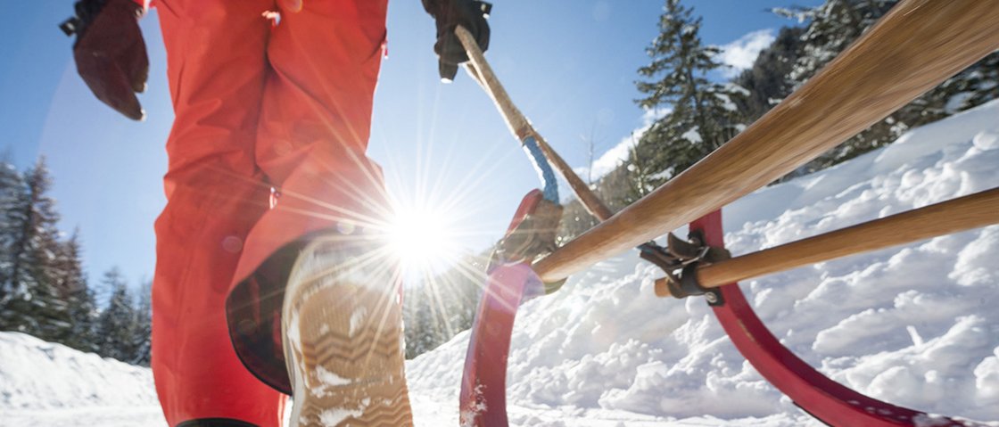 Das Plus im Skiurlaub im Stubaital Person in oranger Winterkleidung zieht einen roten Schlitten im Schnee bei Sonnenschein