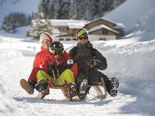 Qualitätszeit im Familienhotel im Stubaital Familie fährt Schlitten auf schneebedecktem Weg im Winter