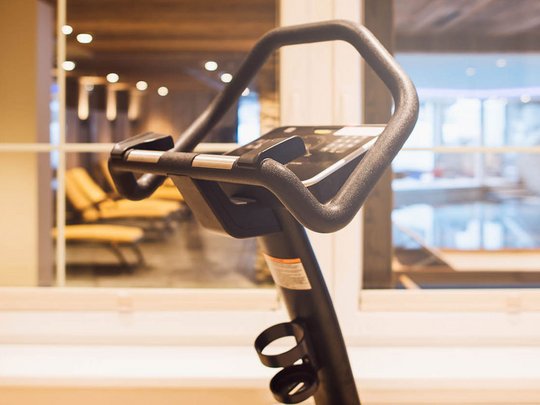 Fit bleiben im Sporthotel im Stubaital Fitnessfahrrad im Fitnessraum mit Blick auf Liegestühle und Fenster