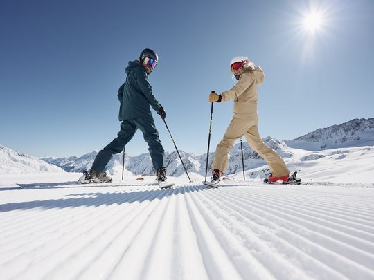 Dreaming of skiing? Head to our ski hotel in Stubaital! Two skiers looking back on freshly groomed slope under sunny sky