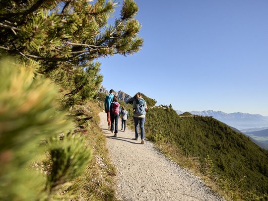 Qualitätszeit im Familienhotel im Stubaital Familie wandert auf Bergweg bei klarem Himmel und grüner Landschaft