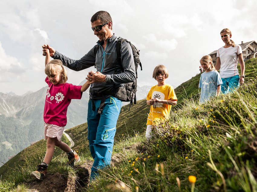 Qualitätszeit im Familienhotel im Stubaital Familie wandert mit Kindern auf einem Bergpfad in den Alpen bei bewölktem Himmel