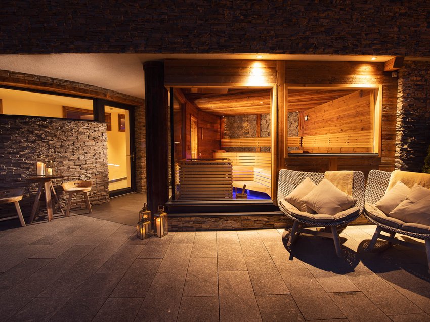 Unwind at our spa hotel in Stubaital Lit outdoor area with sauna window and cozy chairs at night