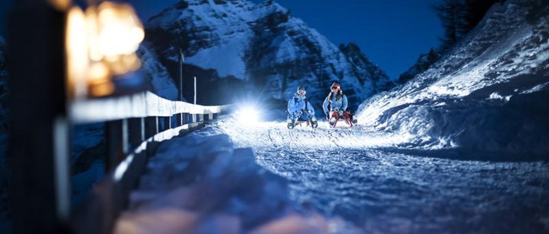That little extra on your ski holiday in Stubaital Two people sledding at night on a snowy mountain path