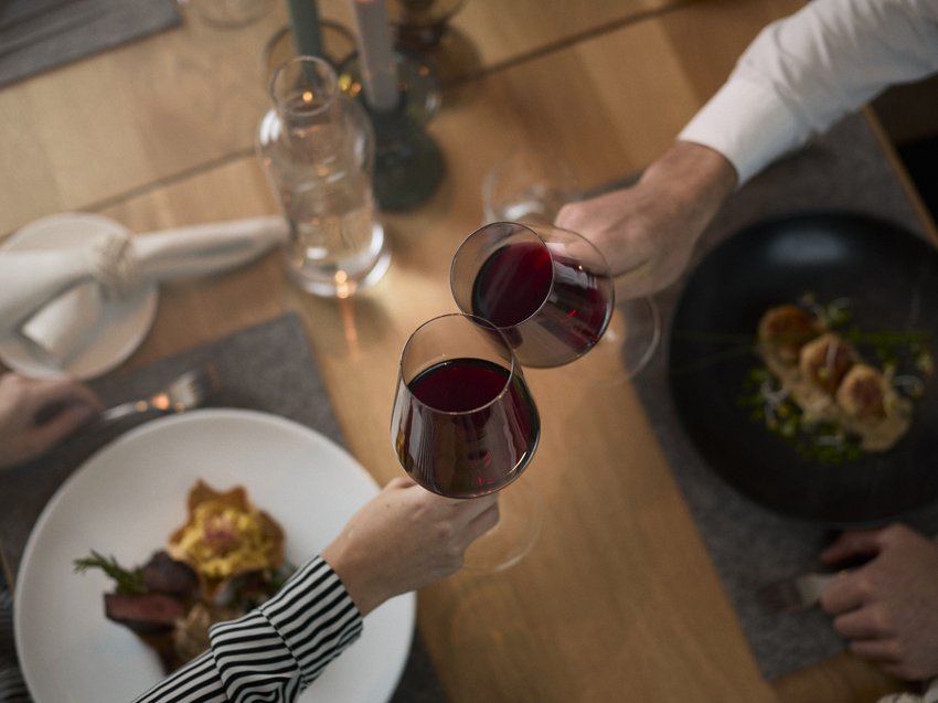 Köstlichkeiten im Berkönig Zwei Personen stoßen mit Rotweingläsern über einem gedeckten Tisch an