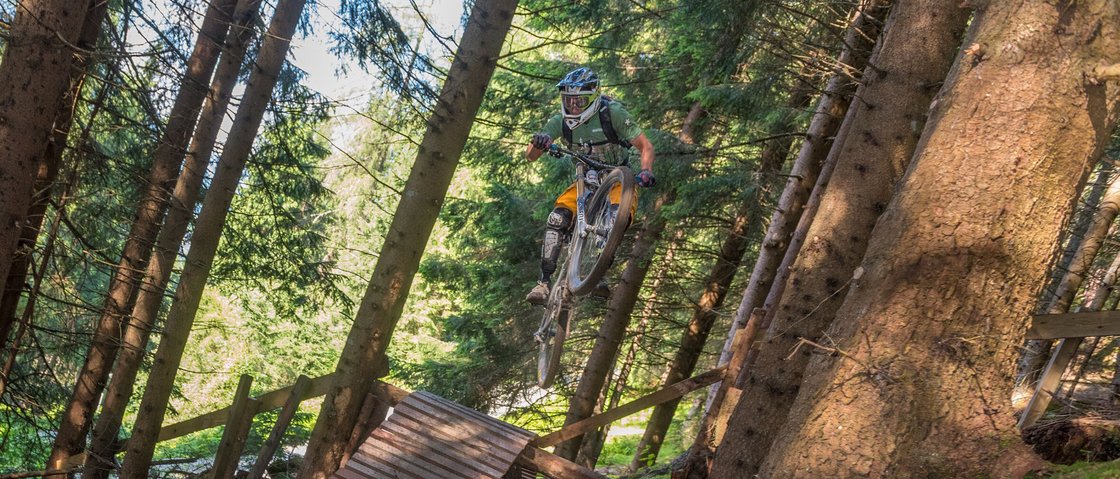 Traumhaft: MTB im Stubaital Mountainbiker springt im Wald von einer Rampe über einen Weg