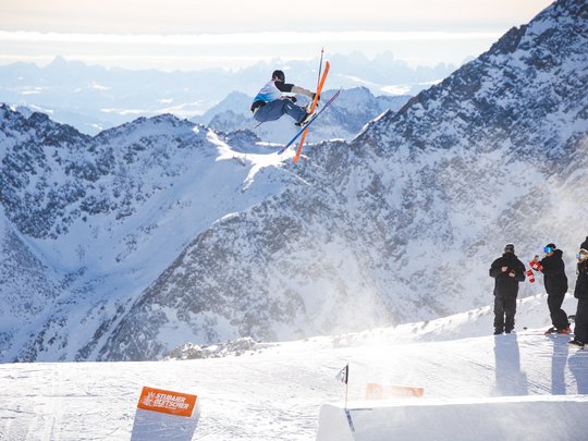 Dreaming of skiing? Head to our ski hotel in Stubaital! Skier jumping high over snow with mountains in background and spectators