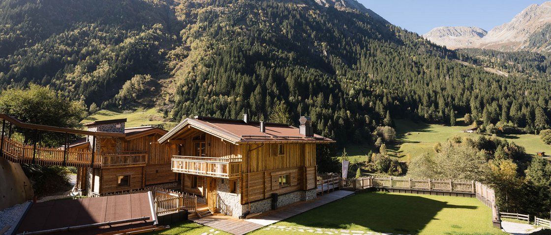 Recharge at our hotel in Neustift im Stubaital, Austria Wooden cabins with mountain backdrop and green lawn on a sunny day
