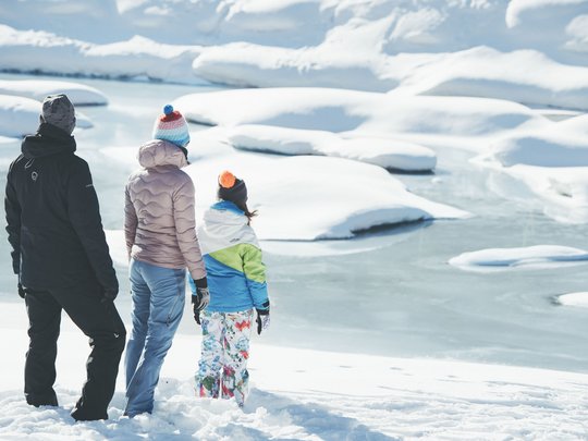 Qualitätszeit im Familienhotel im Stubaital Drei Personen in Winterkleidung stehen im Schnee und blicken auf einen zugefrorenen See
