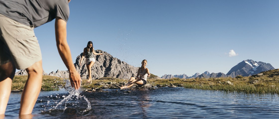 Love for nature at our hiking hotel in Stubaital Three people splashing water in a mountain lake with clear sky and mountains