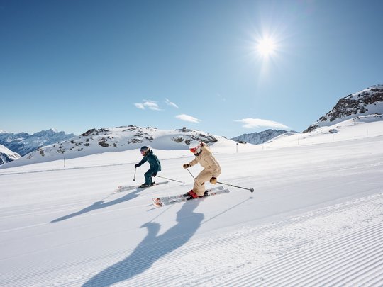 Dreaming of skiing? Head to our ski hotel in Stubaital! Two skiers on a freshly groomed slope under a sunny sky in the mountains