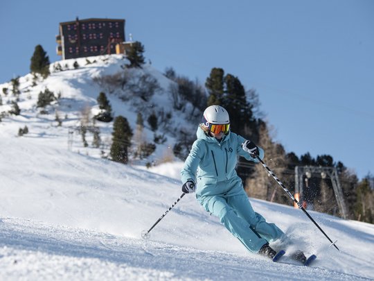 Dreaming of skiing? Head to our ski hotel in Stubaital! Skier in blue outfit skiing on snowy slope under clear blue sky
