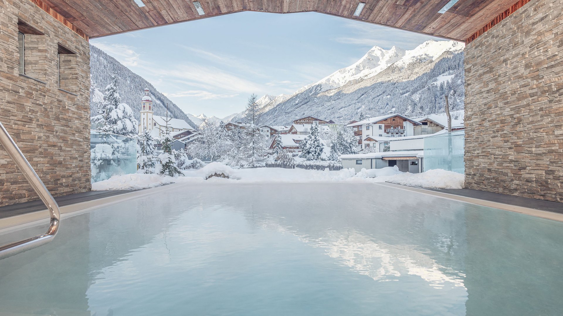 Sich erholen im Hotel in Neustift im Stubaital Blick auf winterliches Bergdorf von einem beheizten Außenpool mit Steinmauern