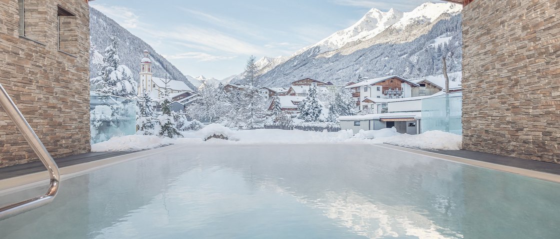 Unwind at our spa hotel in Stubaital View of snowy mountain village from heated outdoor pool with stone walls
