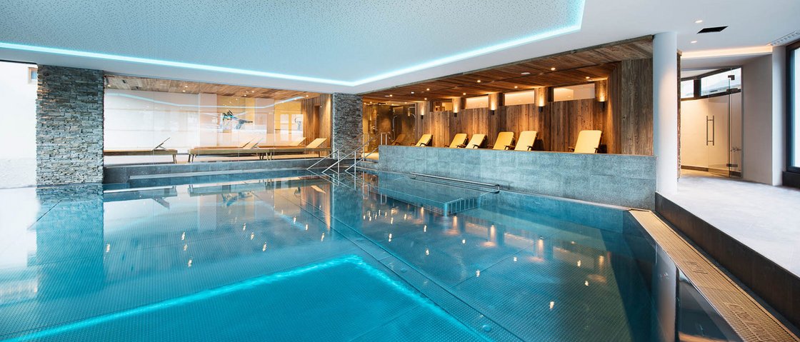 Unwind at our spa hotel in Stubaital Modern indoor pool with lounge chairs and wooden wall paneling