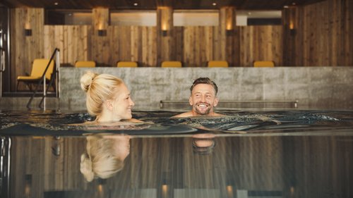Sich erholen im Hotel in Neustift im Stubaital Paar entspannt im Innenpool mit Holzverkleidung und gelben Stühlen