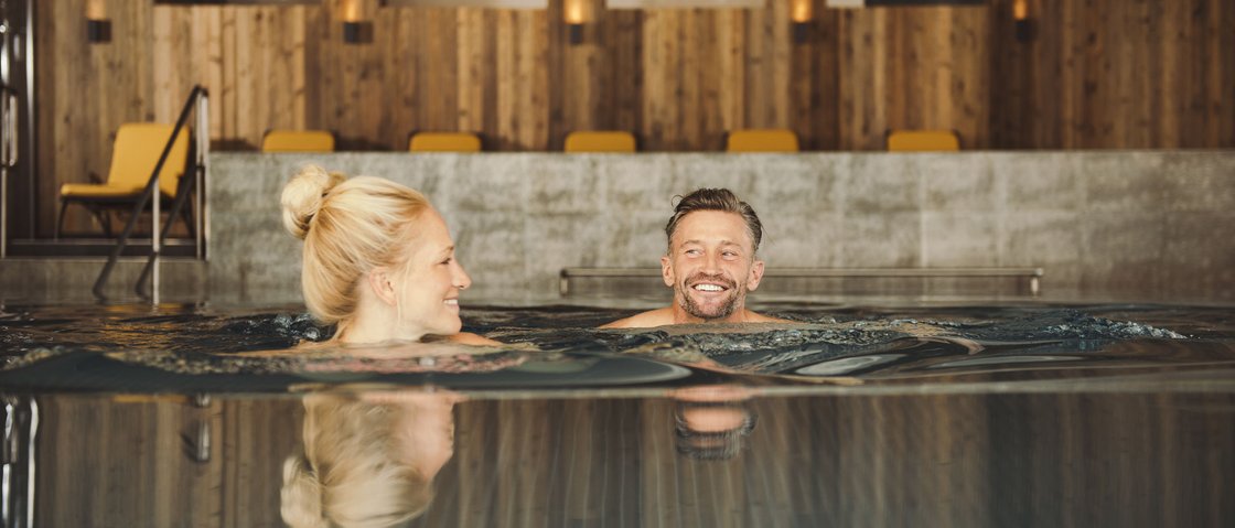Rejuvenation at our 4-star wellness hotel in Tyrol Couple relaxing in indoor pool with wooden walls and yellow chairs