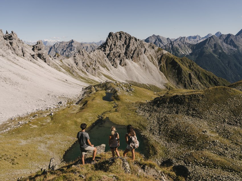 Love for nature at our hiking hotel in Stubaital Three hikers overlooking alpine landscape with mountains and small lake